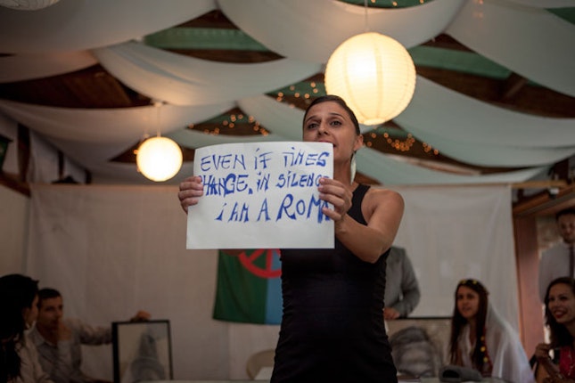 Woman holding a sign that reads, “Even if times change, in silence I am a Roma.”