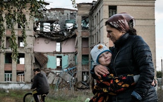 A woman hugging a child in front of a destroyed building