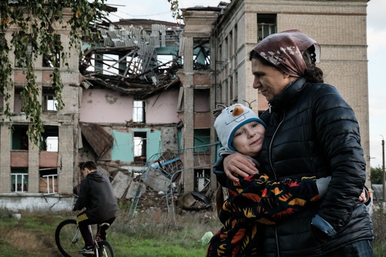 A woman hugging a child in front of a destroyed building