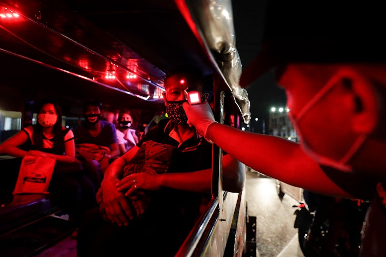 A police officer checks the temperatures of passengers in an effort to slow the spread of COVID-19 in Manila, Philippines, on March 16, 2020. Photo credit: © Aaron Favila/AP A police officer points a digital thermometer at a person sitting in a vehicle