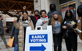 Young people gather outside of a polling station and stand behind an early voting sign.