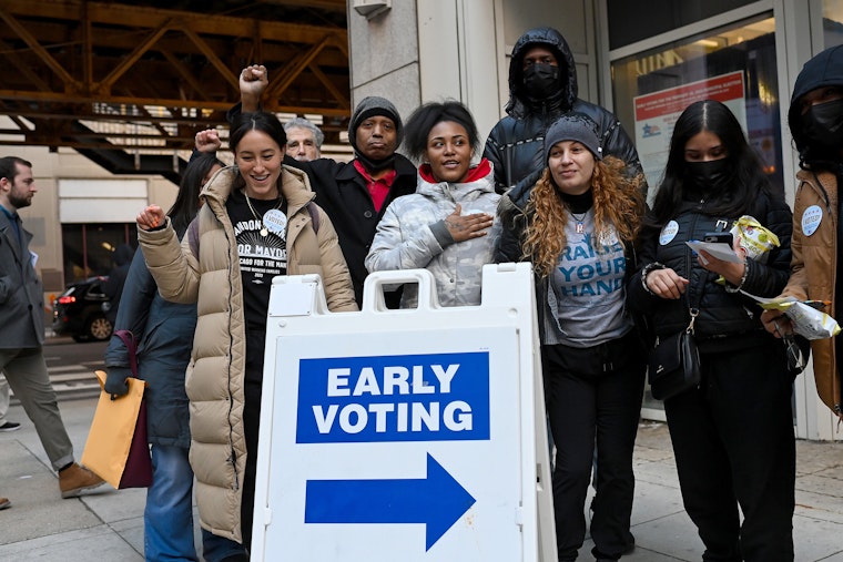 Young people gather outside of a polling station and stand behind an early voting sign.