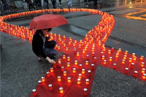 A woman in Belgrade, Serbia, lights a candle on May 15, 2011, in remembrance of individuals who lost their lives to AIDS. Photo credit: © Alexa Stankovic/AFP/Getty A red ribbon lined with candles on pavement