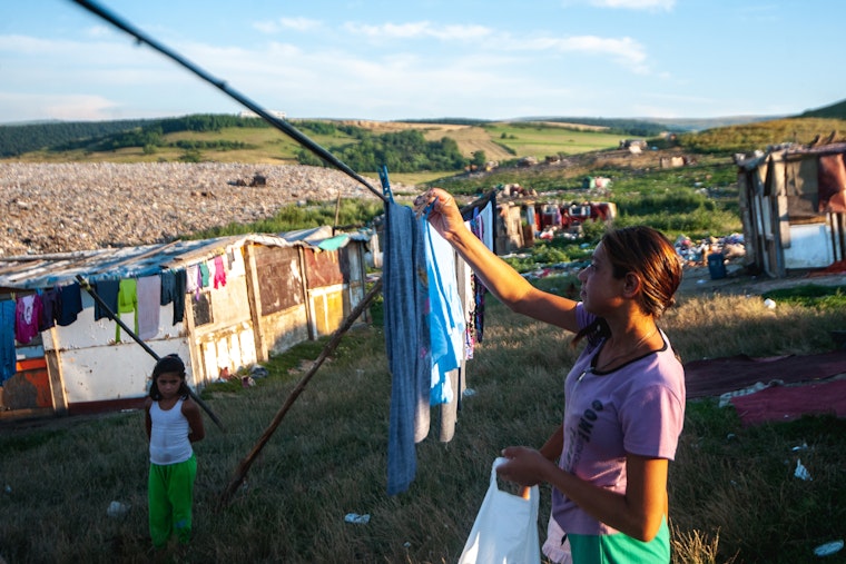 A young woman hangs laundry next to a landfill