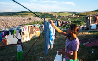 A young woman hangs laundry next to a landfill
