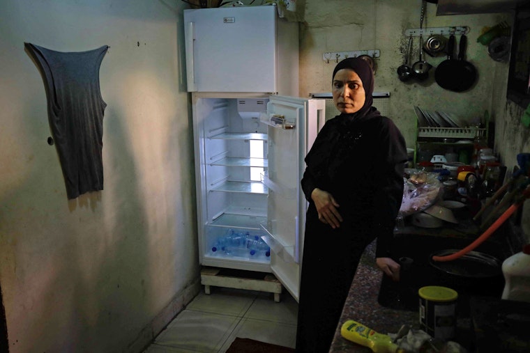 A woman stands in front of an empty refrigerator.