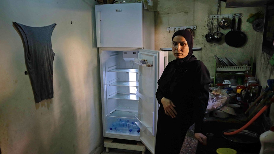 A woman stands in front of an empty refrigerator.
