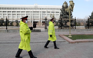 Two police officers in face masks walk in front of an ornate fence surrounding a government building