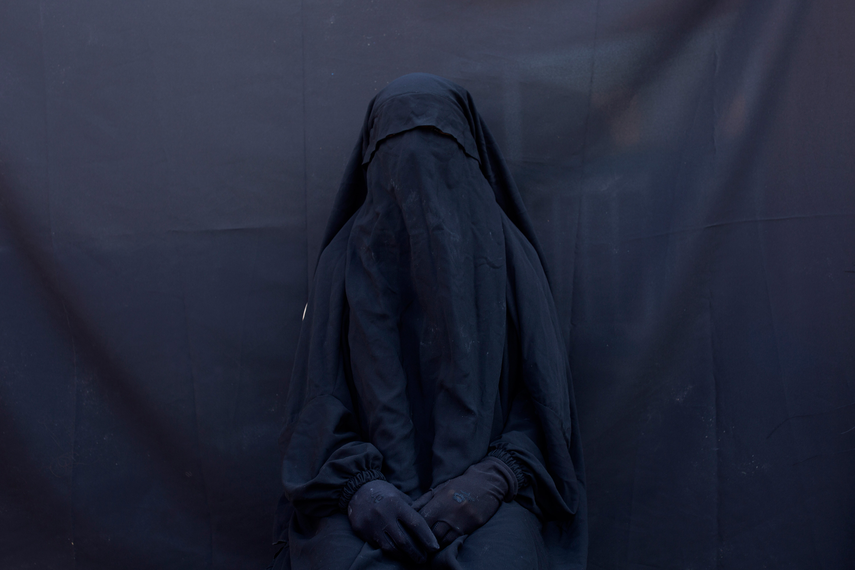 A woman sits in a full face veil and abaya