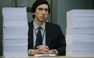 Adam Driver sitting with large stacks of paper in front of him