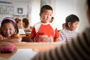 A child standing at a desk in a classroom