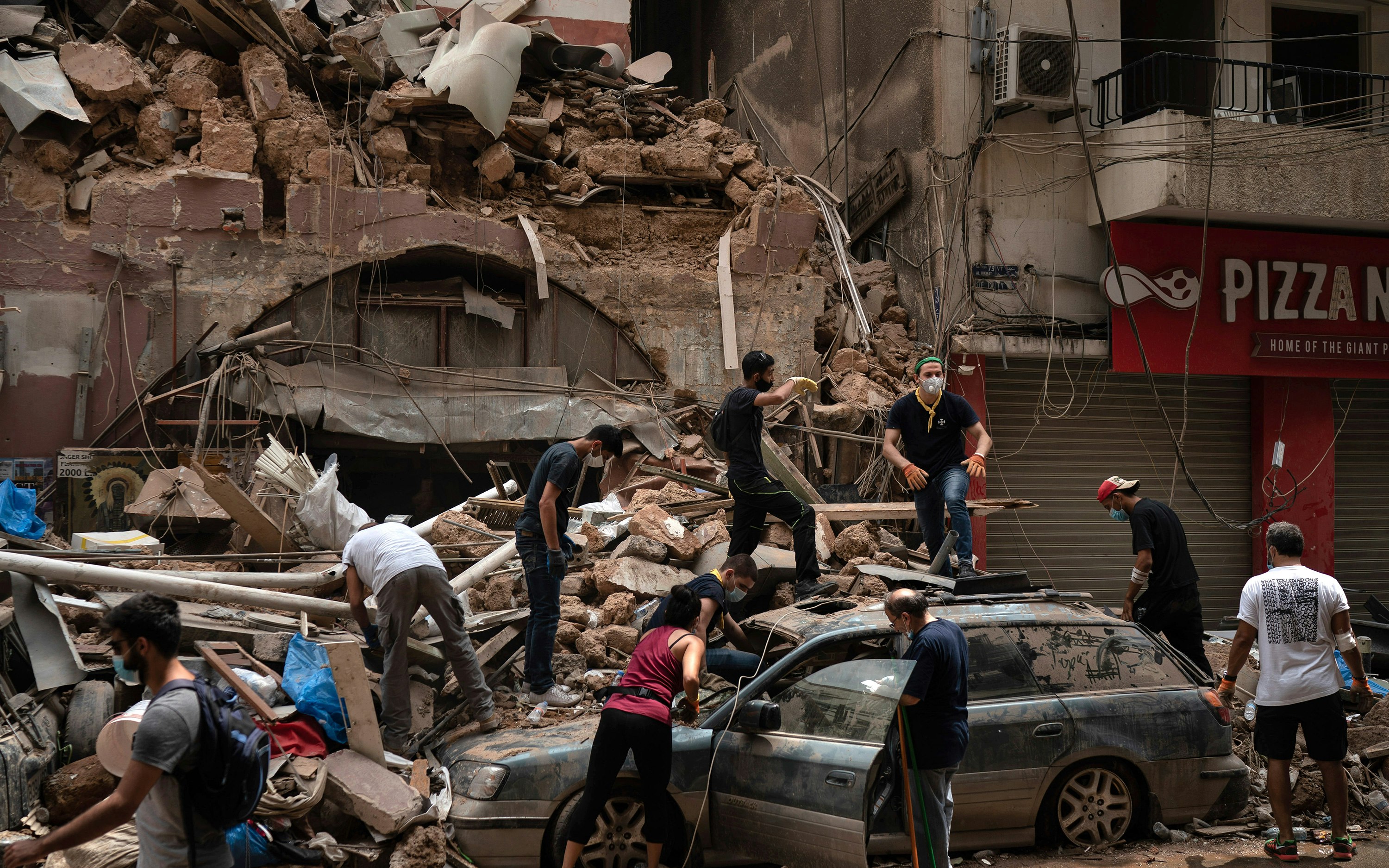People removing debris from a heavily damaged building and car