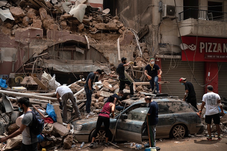 People removing debris from a heavily damaged building and car