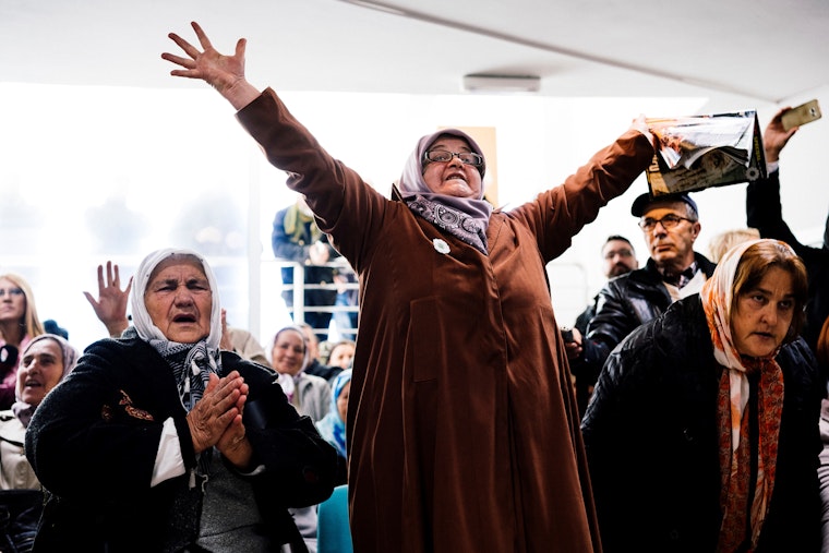 A group of people who are watching a UN court deliver its ruling on TV celebrate by either holding their arms aloft or putting their hands together in prayer.