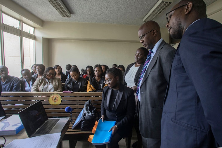 Kenyan lawyers stand around a computer for a virtual meeting.