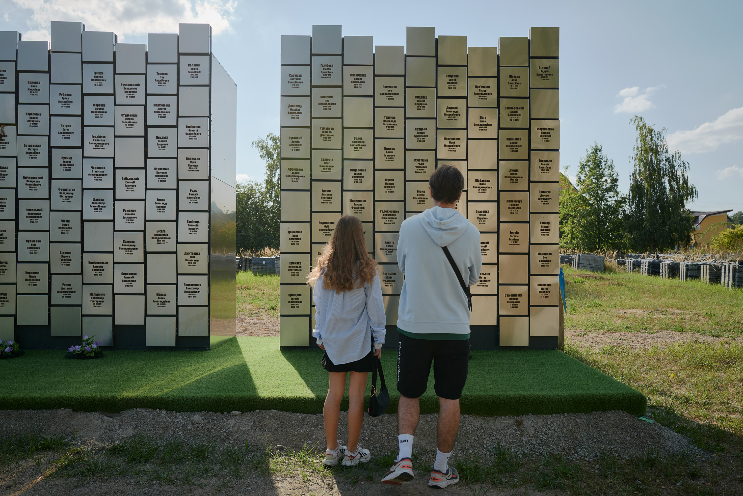 Two people stand looking at a memorial