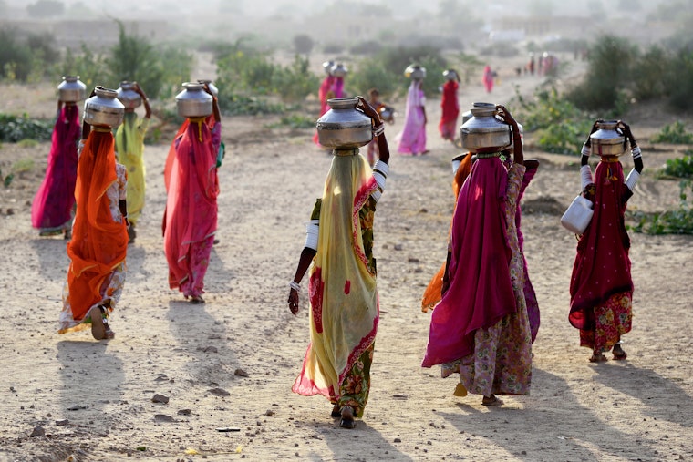 Women in bright saris carrying water jugs on their heads