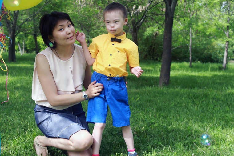Aigul Shakibayeva kneeling next to her son.