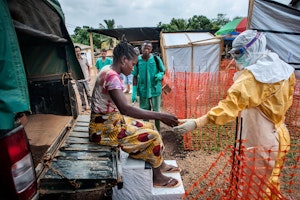 A woman with symptoms of Ebola arrives at a treatment center and is helped by a nurse in protective gear. She is taken to the “suspects” area, where people are quarantined when they show symptoms of the disease but have not been tested. Photo credit: © Sylvain Cherkaoui/Cosmos/MSF A woman being helped out of a truck