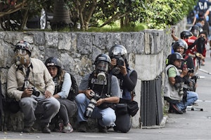 People in gas masks and helmets crouch at a stone wall