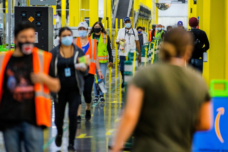 Employees return to their work stations at the Amazon Fulfillment Center in Eastvale, California, on May 20, 2020. Photo credit: © Terry Pierson/Orange County Register/Newscom People wearing vests and masks walk in a line at a warehouse