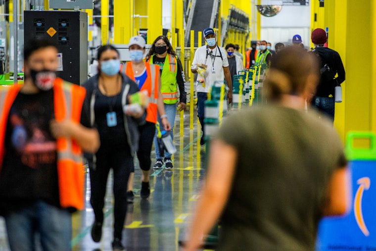 People wearing vests and masks walk in a line at a warehouse