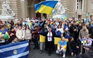 People standing in front of a building holding with Ukrainian flags.