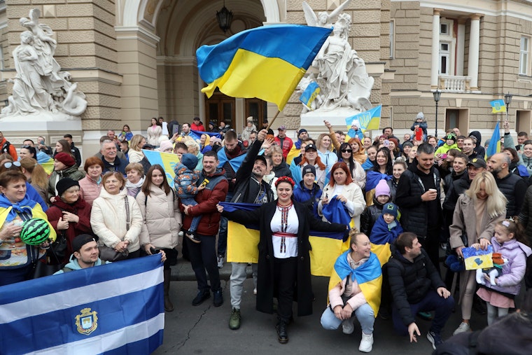 People standing in front of a building holding with Ukrainian flags.