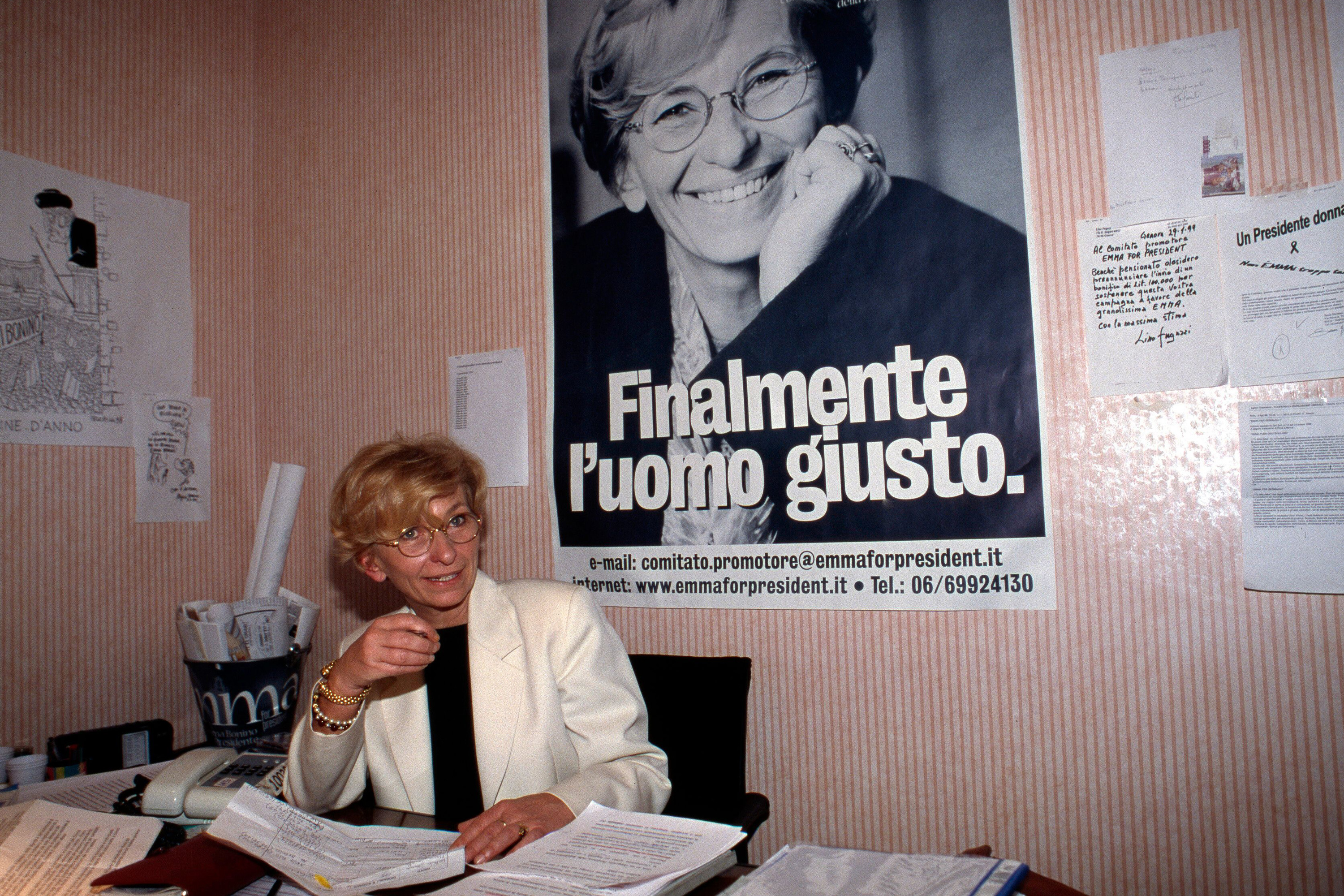 A women sits at a desk in front of a large poster of herself