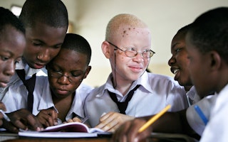 A 15-year-old student with albinism studies next to her friends, in Tanzania. Photo credit: © Dieter Telemans/Panos Pictures A group of students sitting at a desk