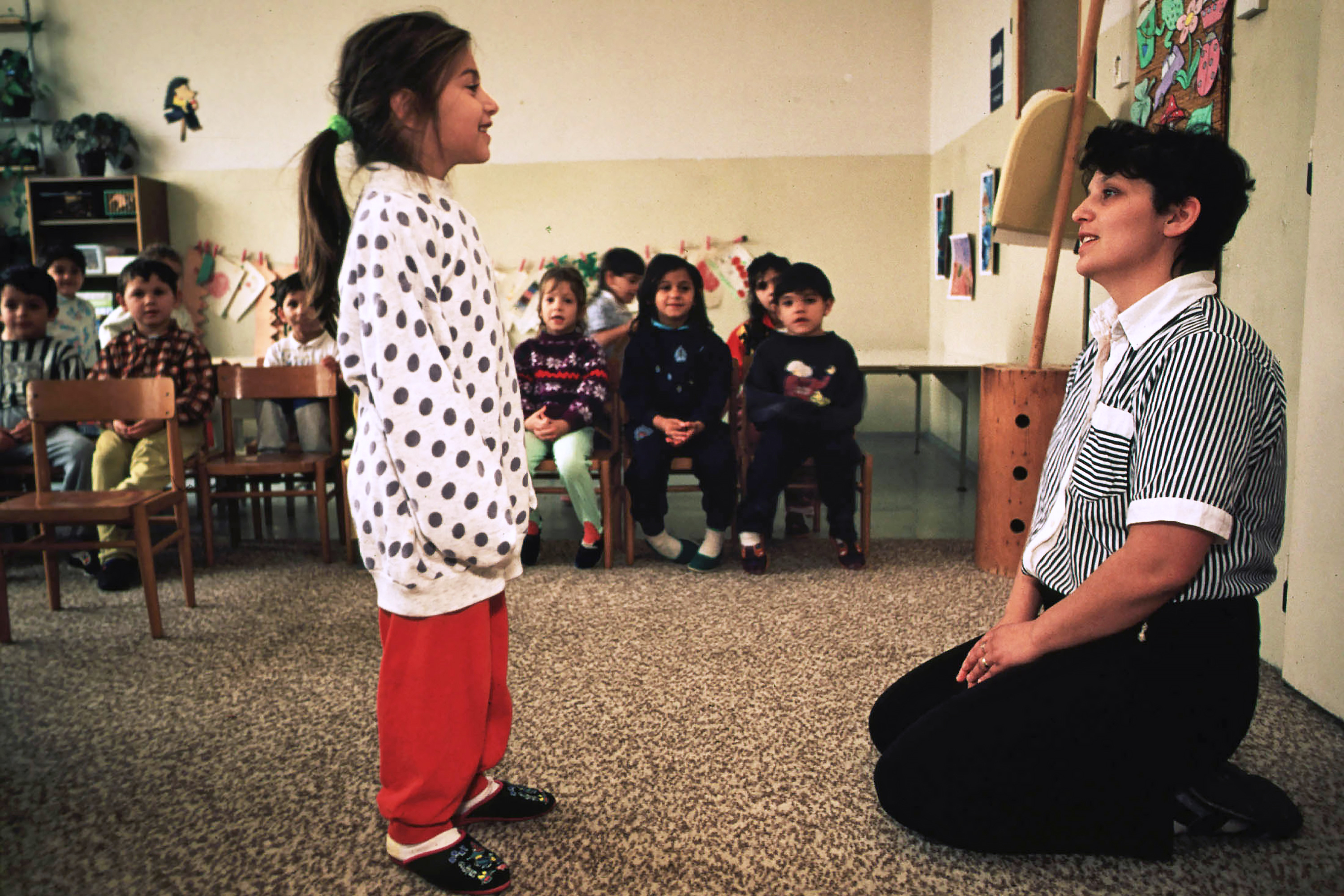 Teacher sitting on ground listening to child