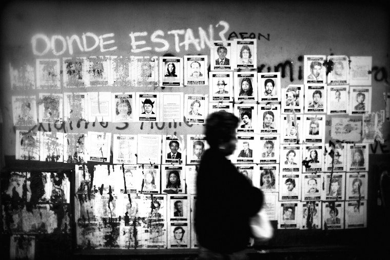 A person walks past a wall pasted with posters