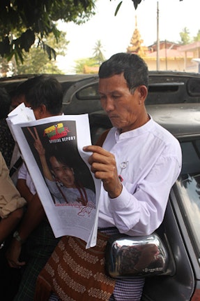 Man reading newspaper with Daw Aung San Suu Kyi on cover