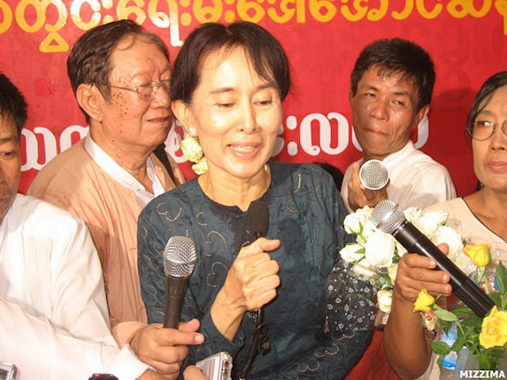 Daw Aung San Suu Kyi at press conference surrounded by reporters holding microphones
