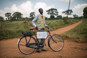 UGANET paralegal William Mulindwa visits the community of Gayaza. Traveling by bicycle, he educates communities living with HIV about their rights and the free legal services available through UGANET. Photo credit: © Sven Torfinn/Panos Pictures for the Open Society Foundations A man standing next to bicycle