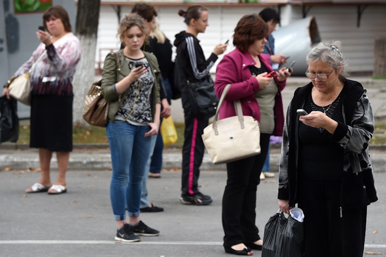 People try to find a signal for their cellphones on a street of Lugansk, in eastern Ukraine, on September 12, 2014. Photo credit: © Philippe Desmazes/AFP/Getty A group of people standing outside and looking at their cellphones