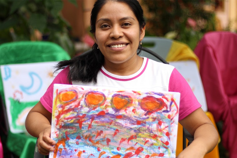 A woman smiles while holding up a piece of artwork