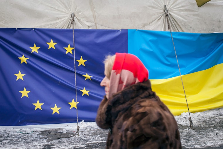 A woman walks past a tent displaying the European Union and Ukrainian flags in Independence Square on January 28, 2014, in Kyiv, Ukraine. Photo credit: © Rob Stothard/Getty A woman walking past flags