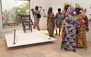Visitors to the Center for Arts and Culture, in Cotonou, Benin, on January 17, 2020. Photo credit: © Prosper Dagnitche/AFP/Getty People standing near a chair and other artifacts on exhibit