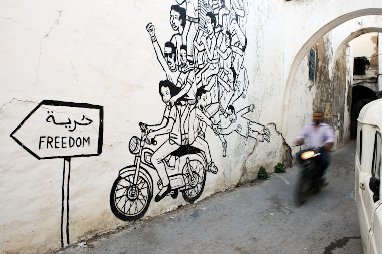 Man on a motorbike rides past wall art of a motorbike.