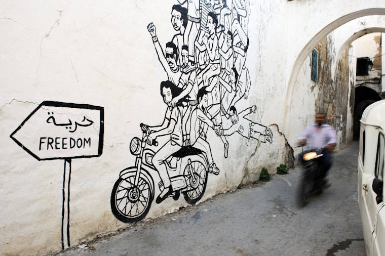A man on his motorbike drives past Arab Spring-inspired street art in Tunis, Tunisia. Photo credit: © Lindsay Mackenzie/Redux Man on a motorbike rides past wall art of a motorbike.