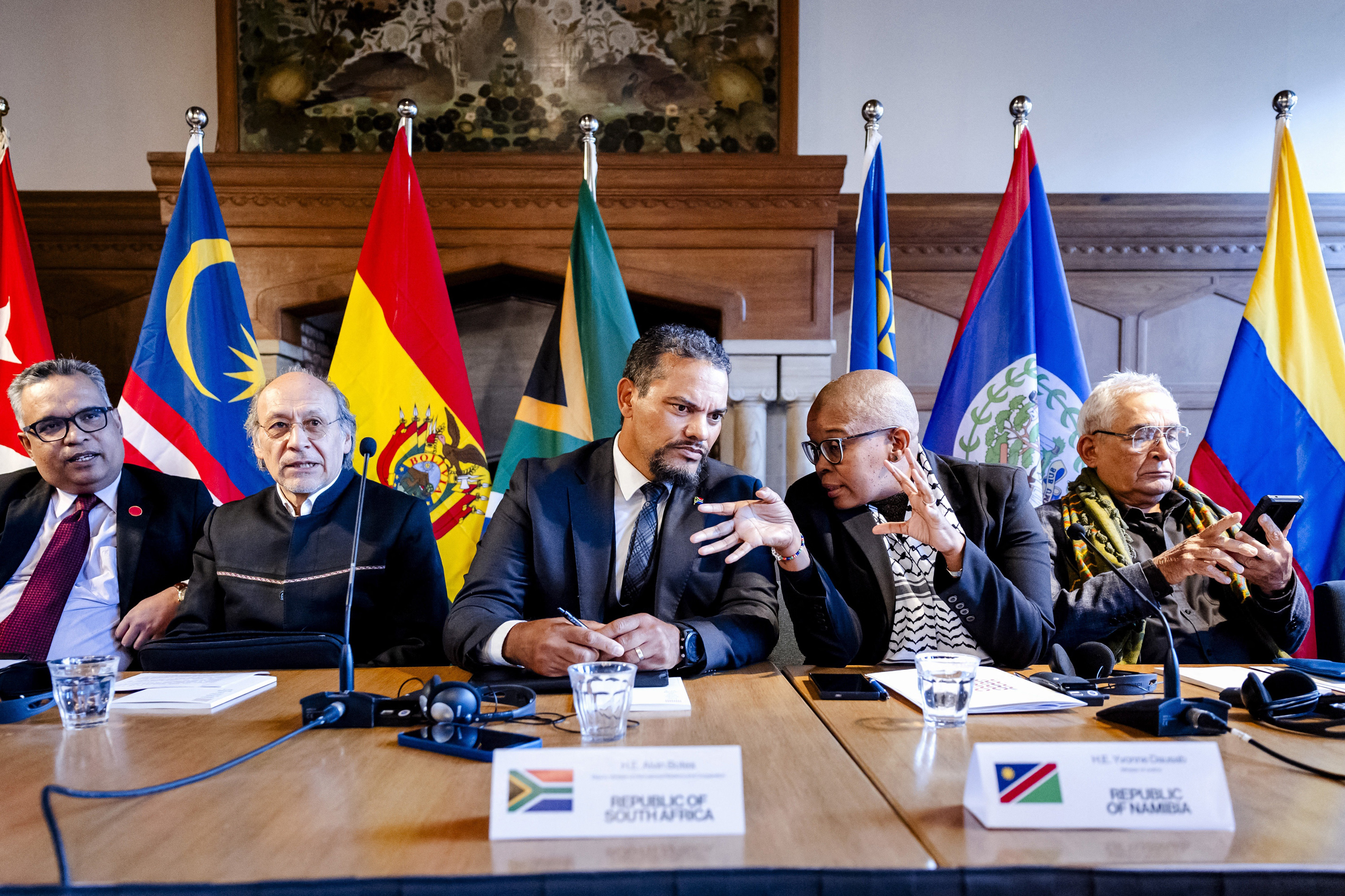 A group of people sit at a meeting table with flags behind them