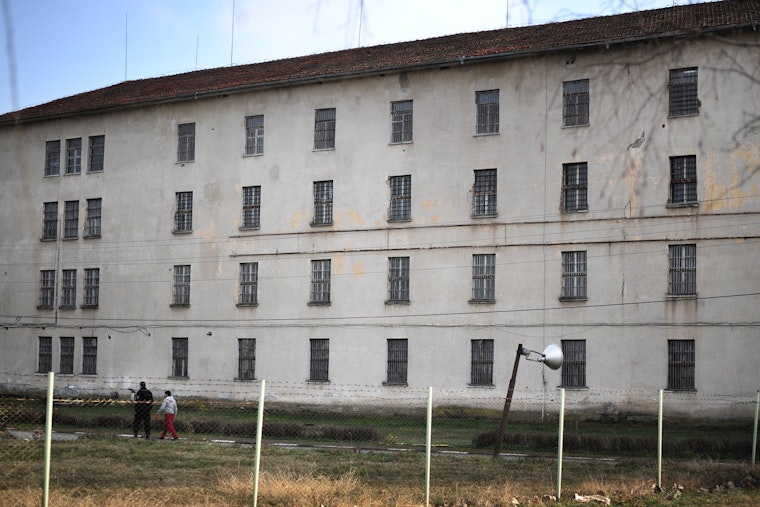 Two people walk near a prison building