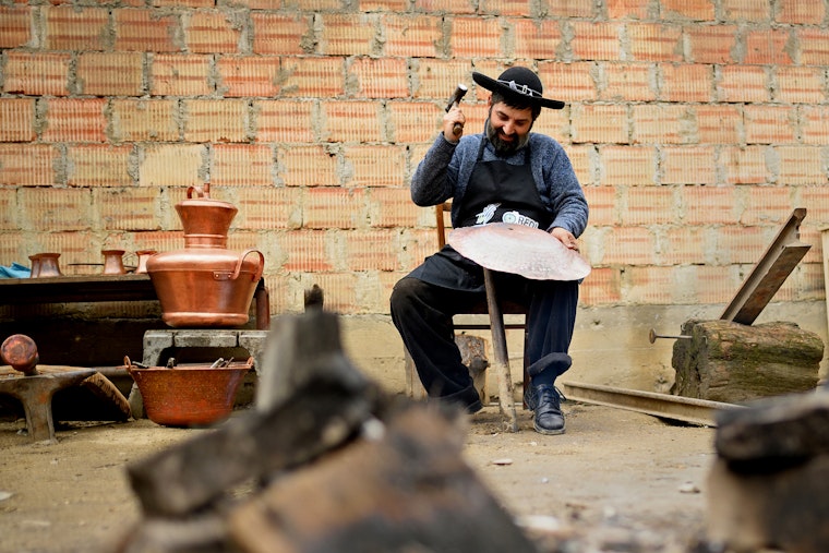 A seated man holding a hammer and a piece of copper