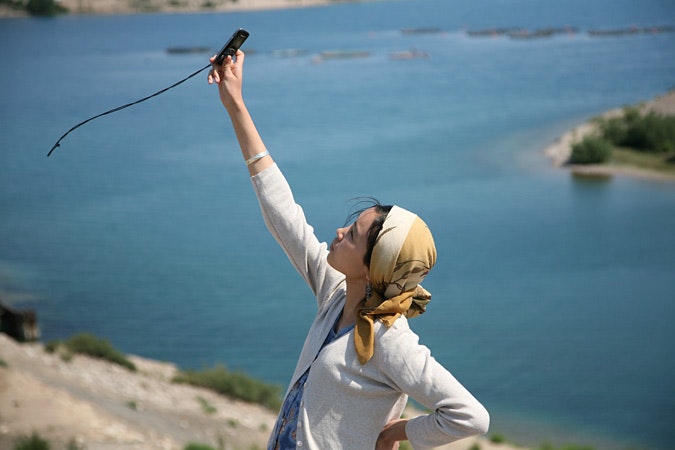 Woman by water with raised arm, holding a cell phone