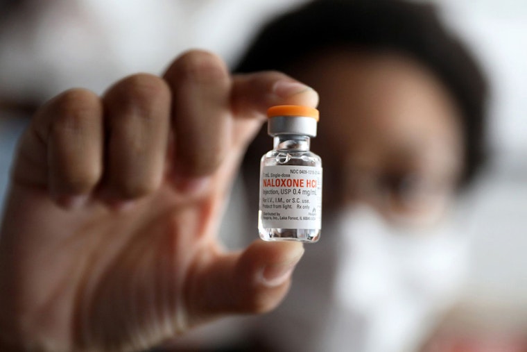 A hand holding a bottle of naloxone