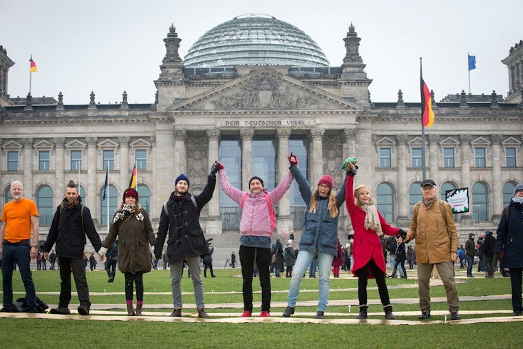 A group of adults holding hands in front of the Reichstag building