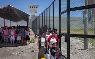 Women and children standing in lines outside a prison fence.
