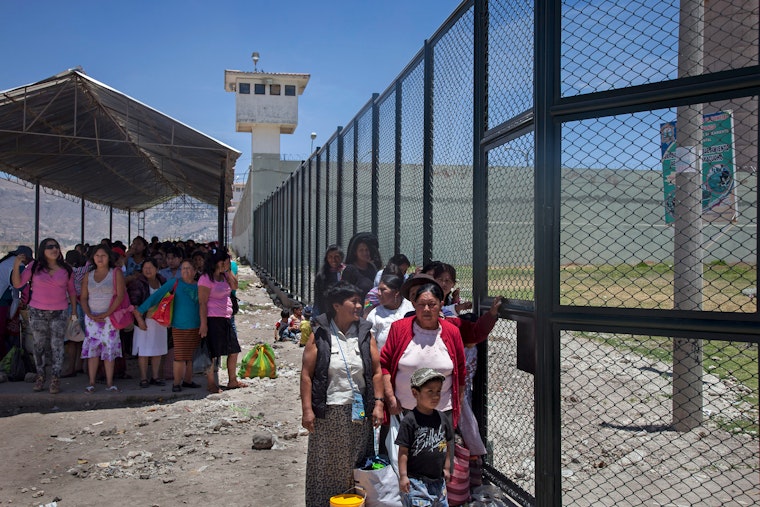 Mujeres y niños parados en fila tras una cerca de la prisión.