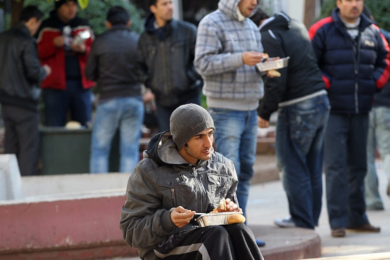 A young man eats outside a soup kitchen in Athens on February 15, 2012. Photo credit: © Orestis Panagiotou/Newscom A man sitting on a bench eating